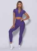 Model facing forward with her left hand on waist  wearing our neon zip top in iris color and a matching leggings
