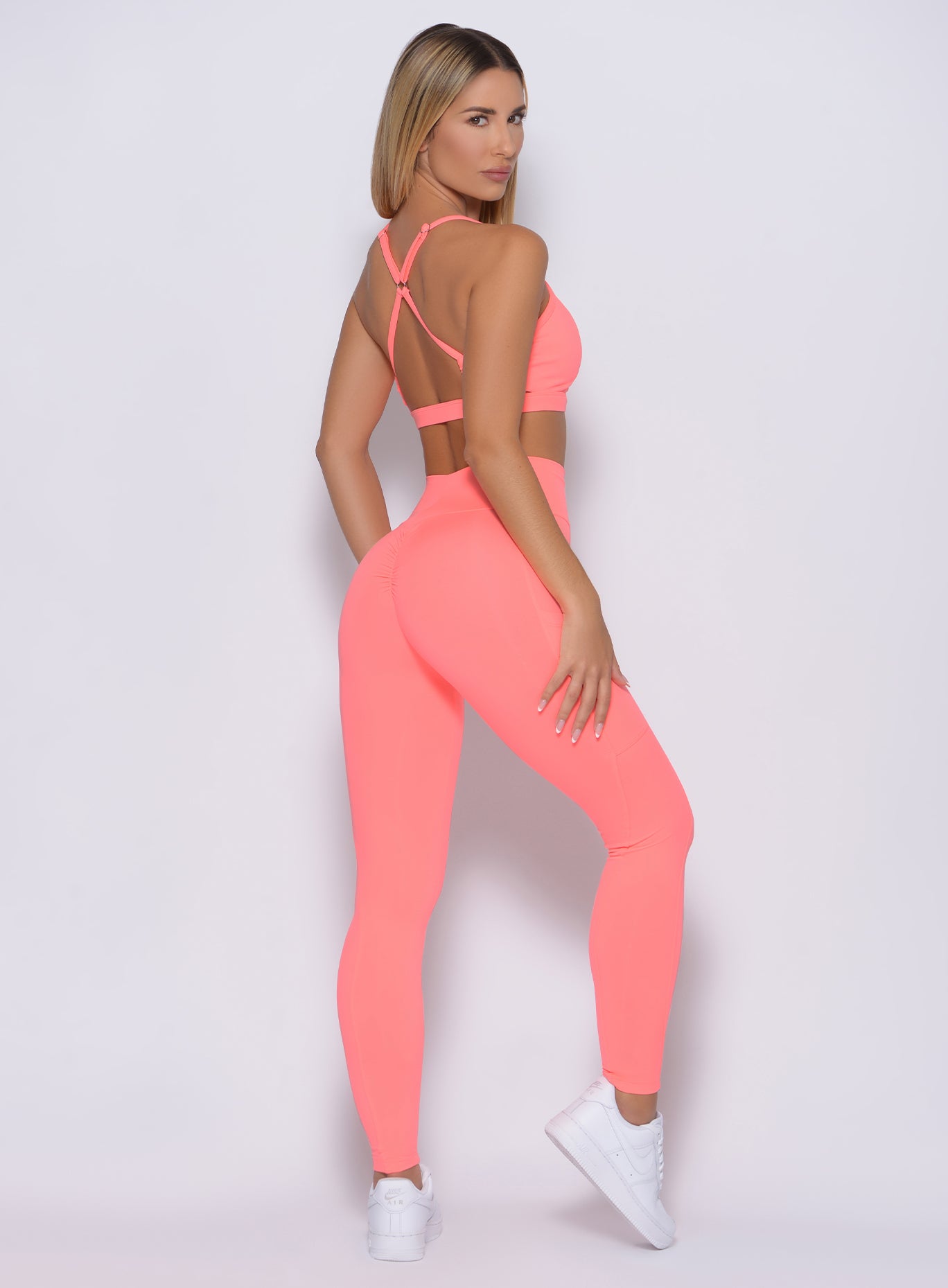 Right side profile view of a model angled right wearing our pumped sports bra in wild peach color and a matching leggings