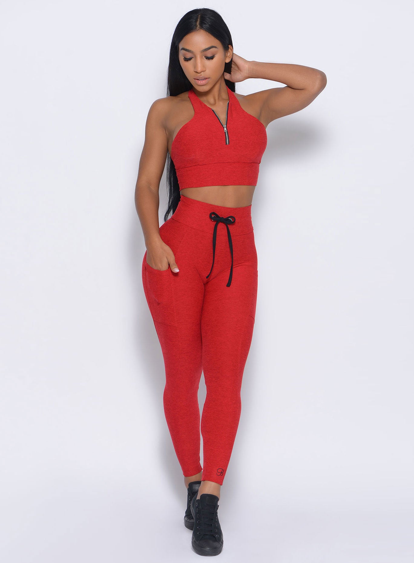 Front profile view of the model with her right hand in pocket wearing our thrive leggings in sunset red color 