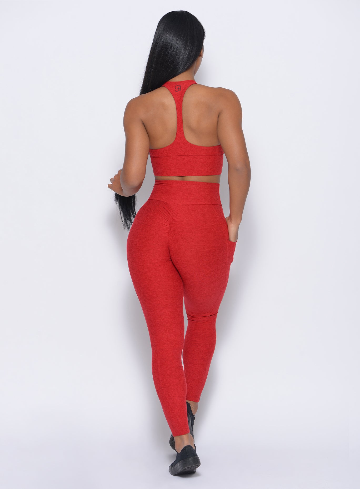 Back profile view of the model wearing our thrive leggings in sunset red color and a matching bra