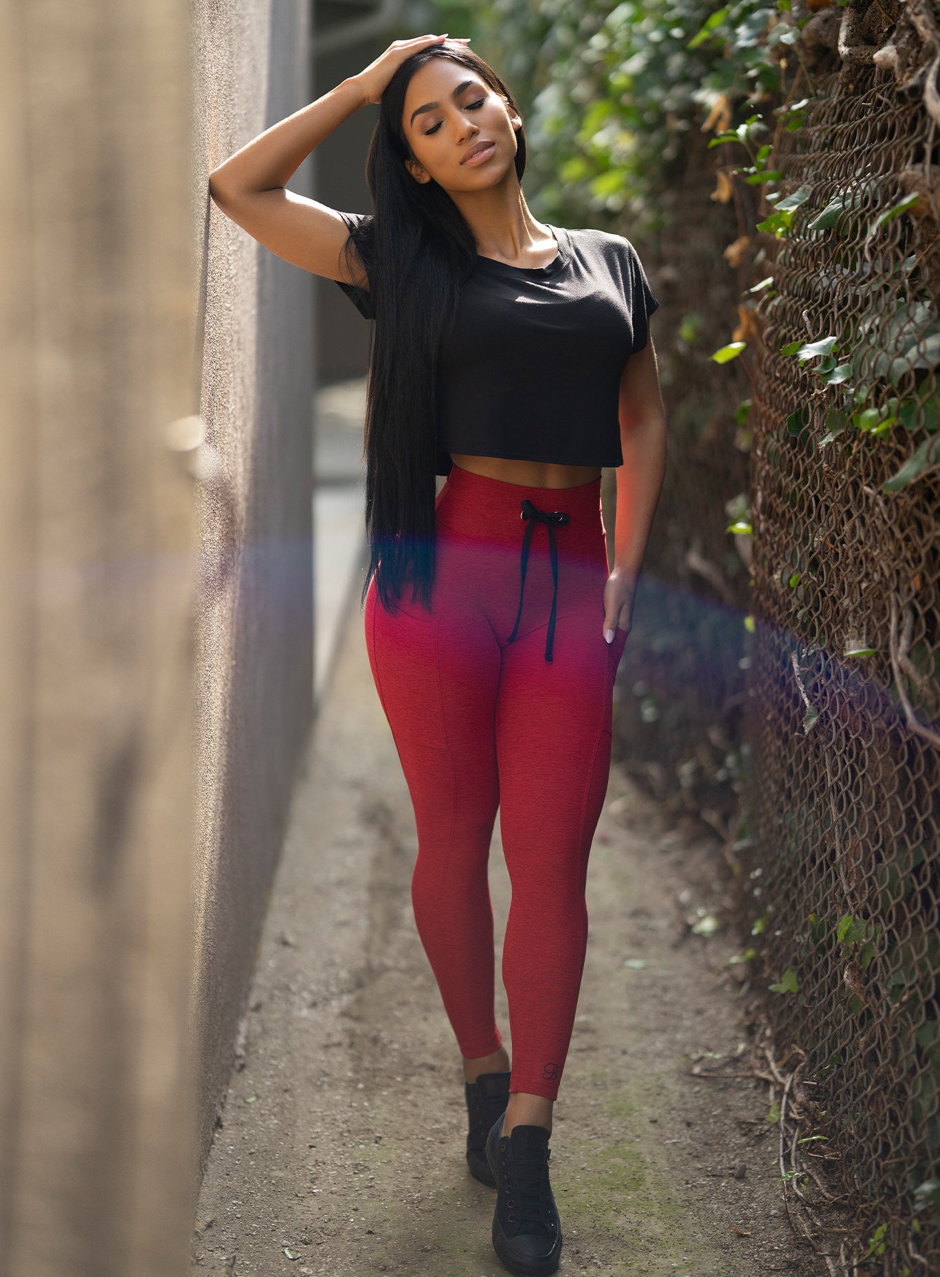 Front view of the model with her right elbow on the wall wearing our thrive leggings in sunset red color and a black top