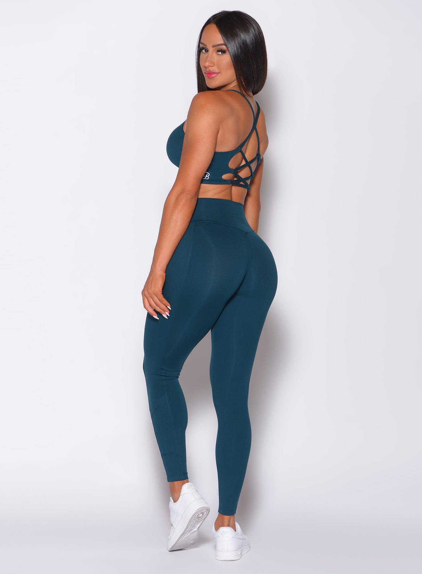 Left side profile view of a model in our empower leggings in peacock color and a matching bra