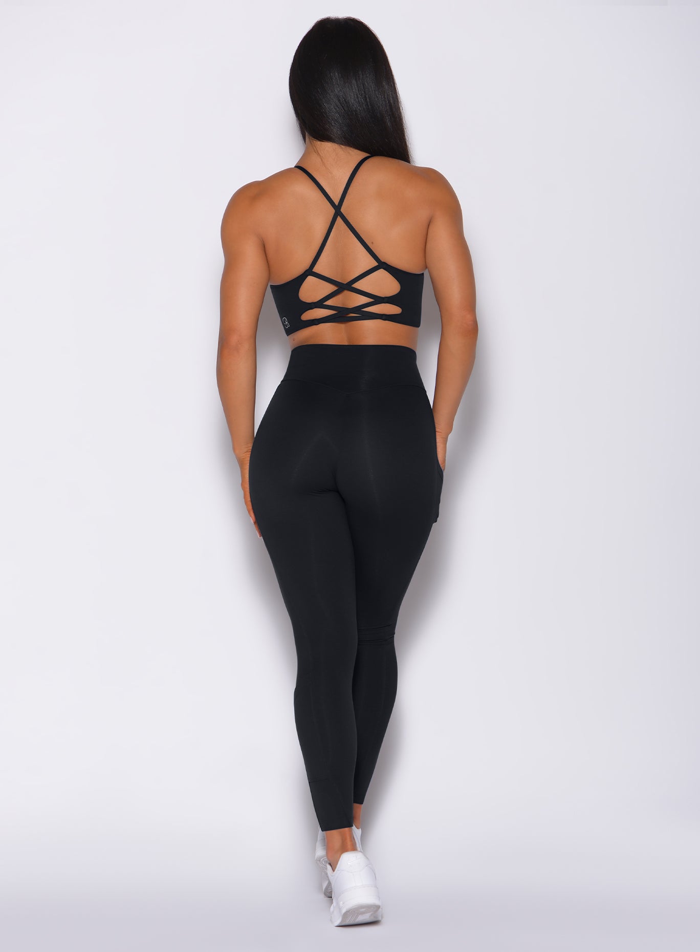 Back profile view of a model wearing our black empower leggings and a matching bra