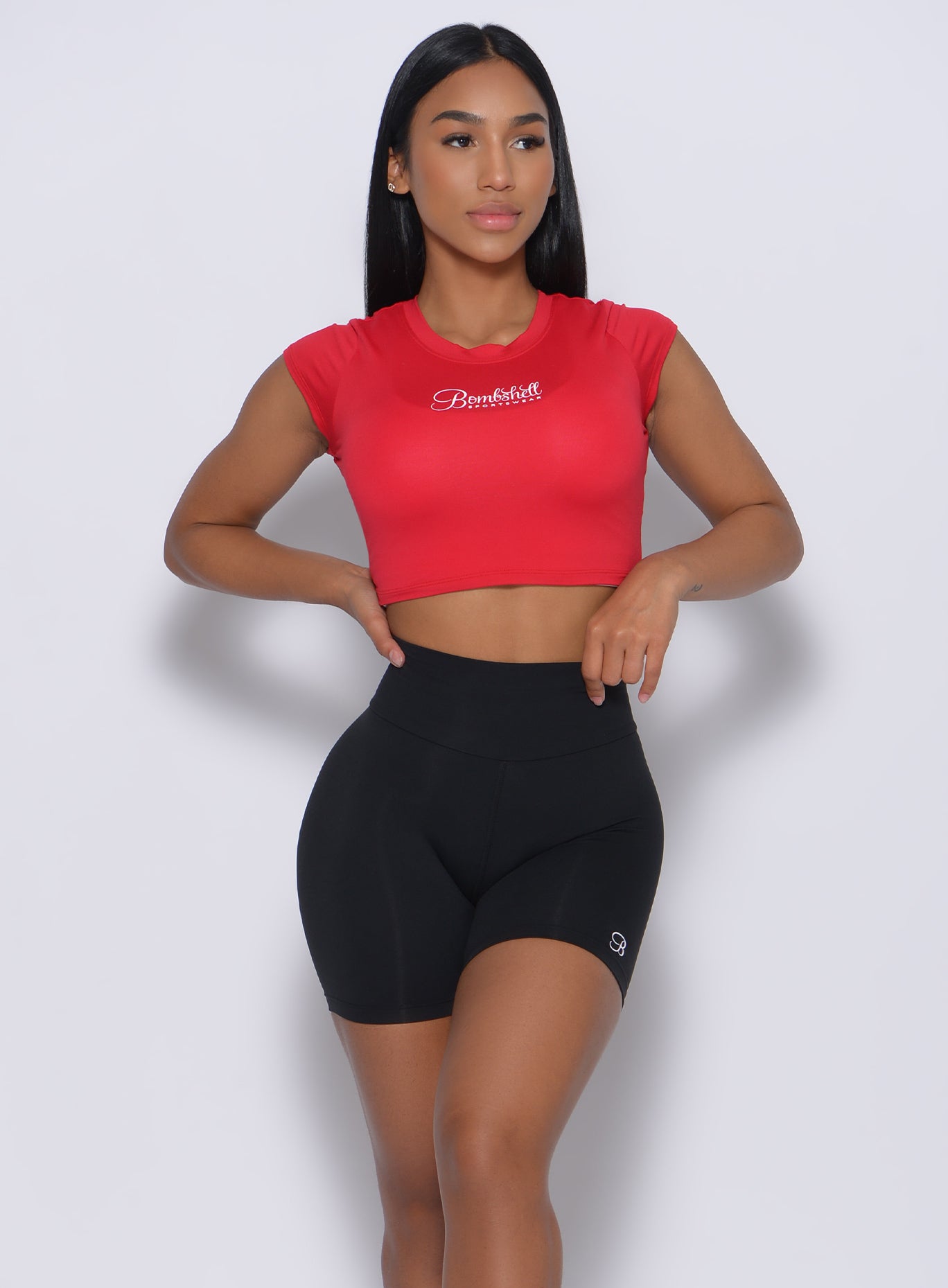 Front profile  view of a model in our crop fit fam tee in apple red color and a black shorts