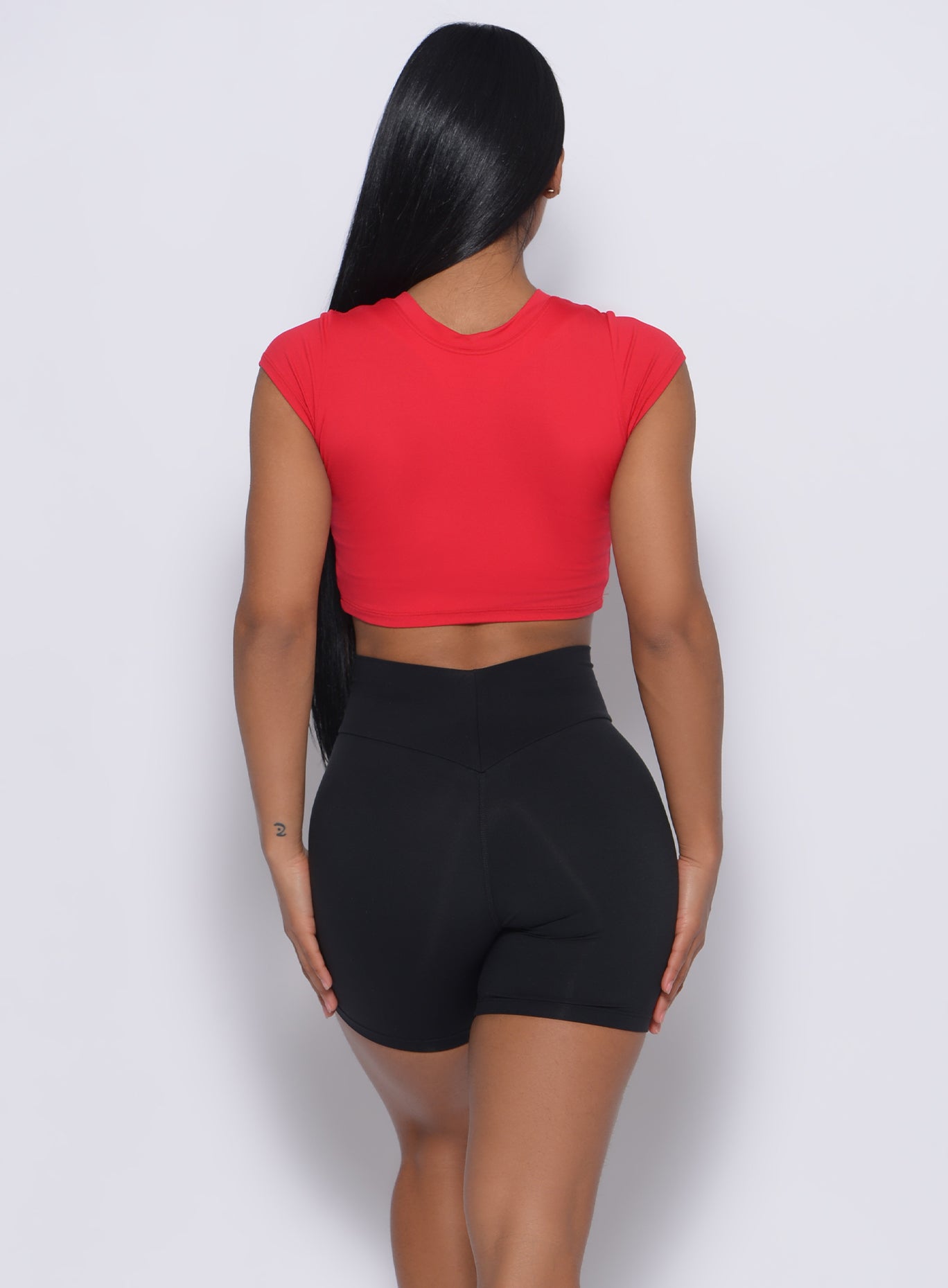 Back profile  view of a model in our crop fit fam tee in apple red color and a black shorts