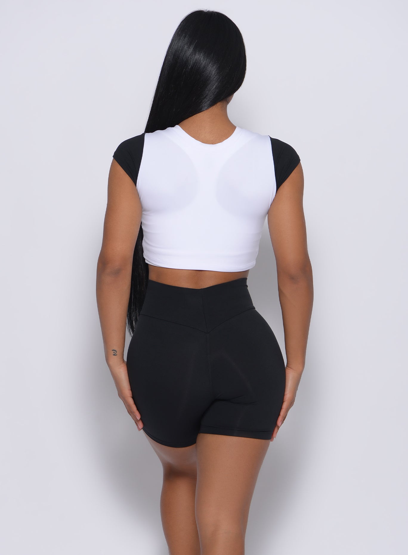 Back profile view of a model wearing our black white crop fit fam tee and a black shorts 