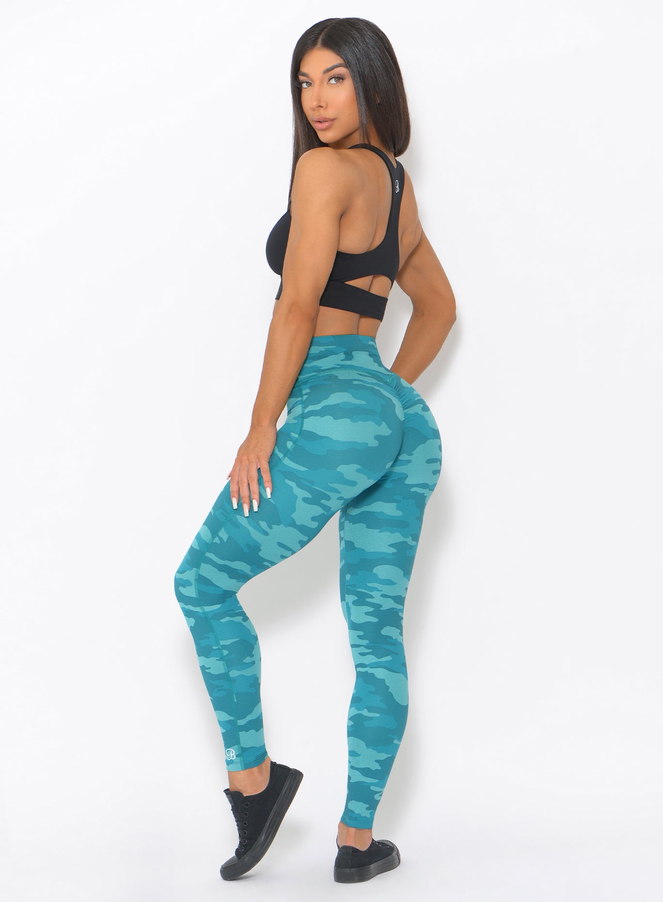 Left side view of the model wearing our fit camo leggings in teal color and a black sports bra