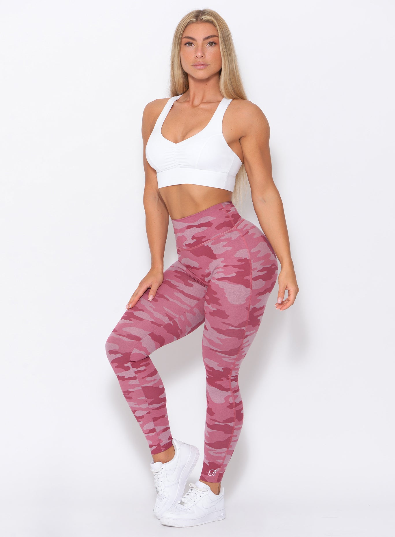 Three quarters view of the model wearing our fit camo leggings in hibiscus camo color and a white bra