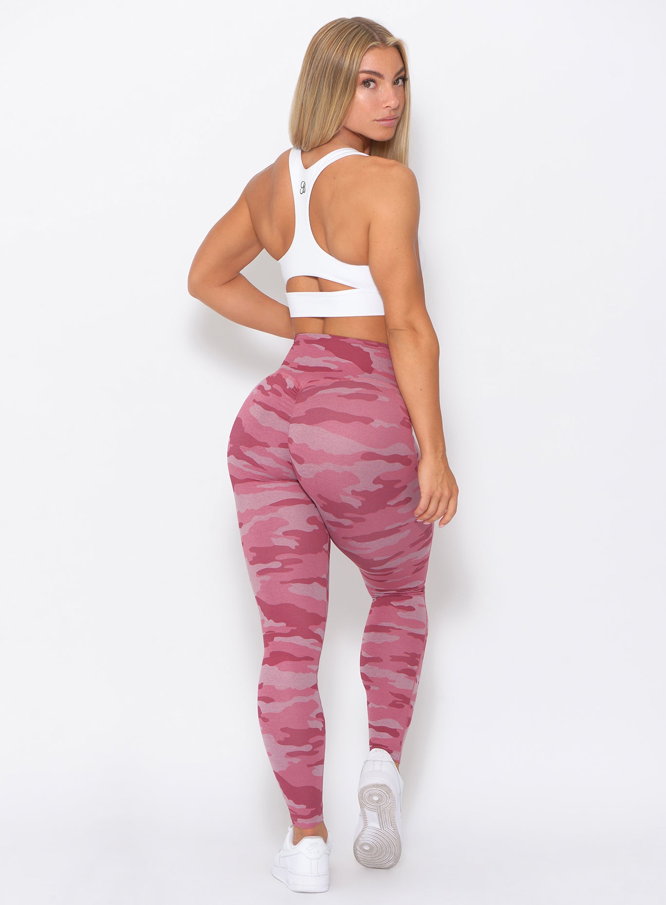 Back view of the model looking backward wearing our fit camo leggings in hibiscus camo color and a white bra