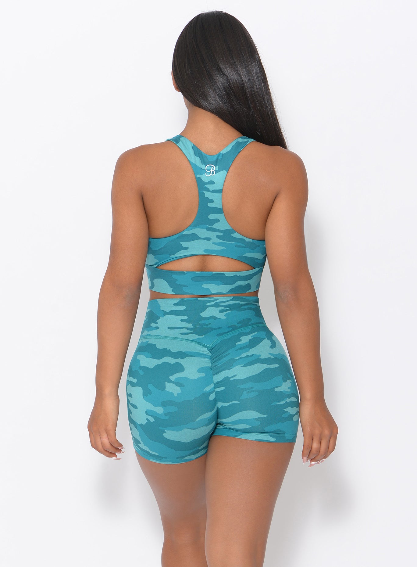 Back view of the model wearing our fit camo shorts in teal color and a matching bra 