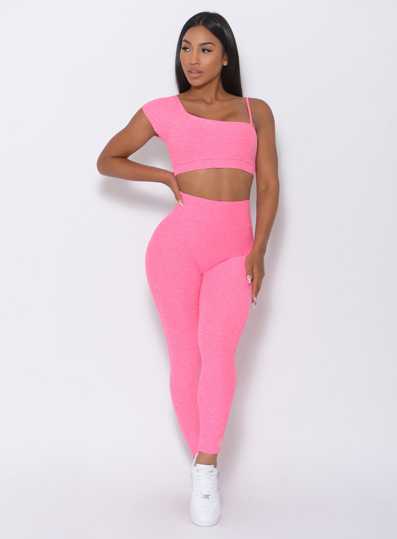 Front view of the model with her right hand on waist wearing our Adore Sports Bra in pink and a matching leggings