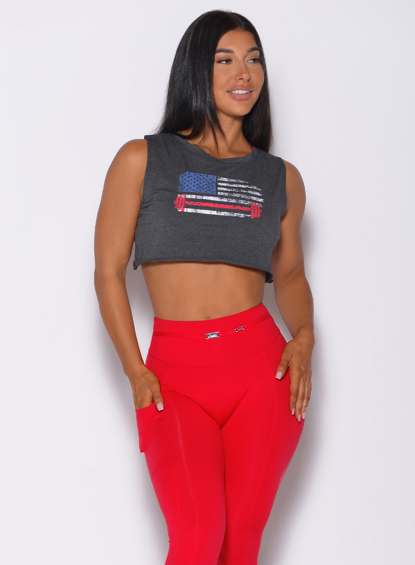 Front profile view of a model with her right hand in pocket wearing  our USA barbell tank in charcoal color and a red leggings