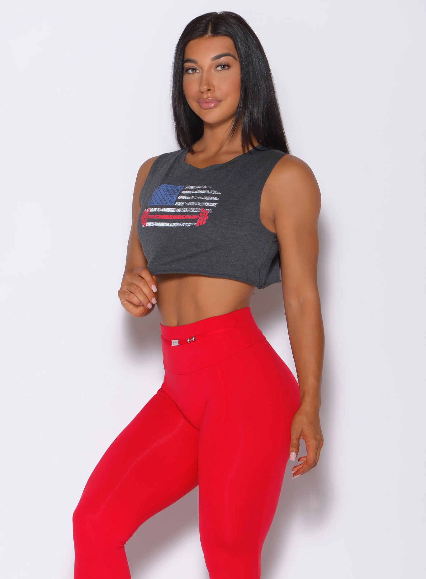 Left side profile view of a model angled left wearing our USA barbell tank in charcoal color and a red leggings