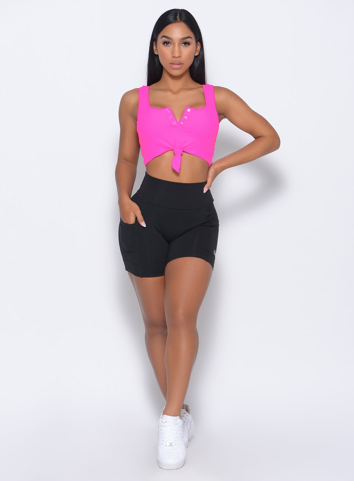 Front profile view of the model with her right hand in pocket wearing our henley sports bra in neon pink and a black shorts 
