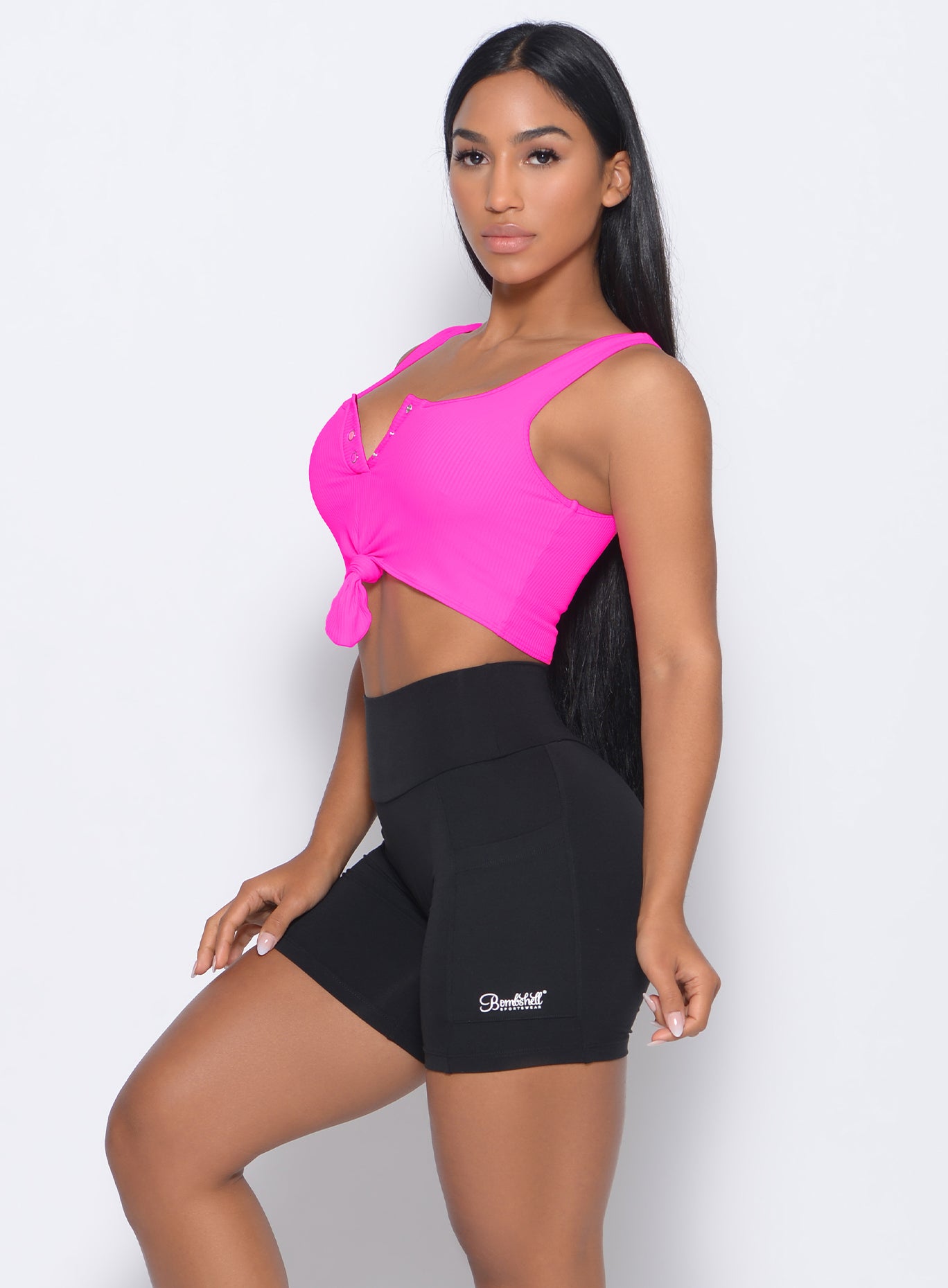 Left side view of the model facing to her left in our henley sports bra in neon pink and a black shorts 