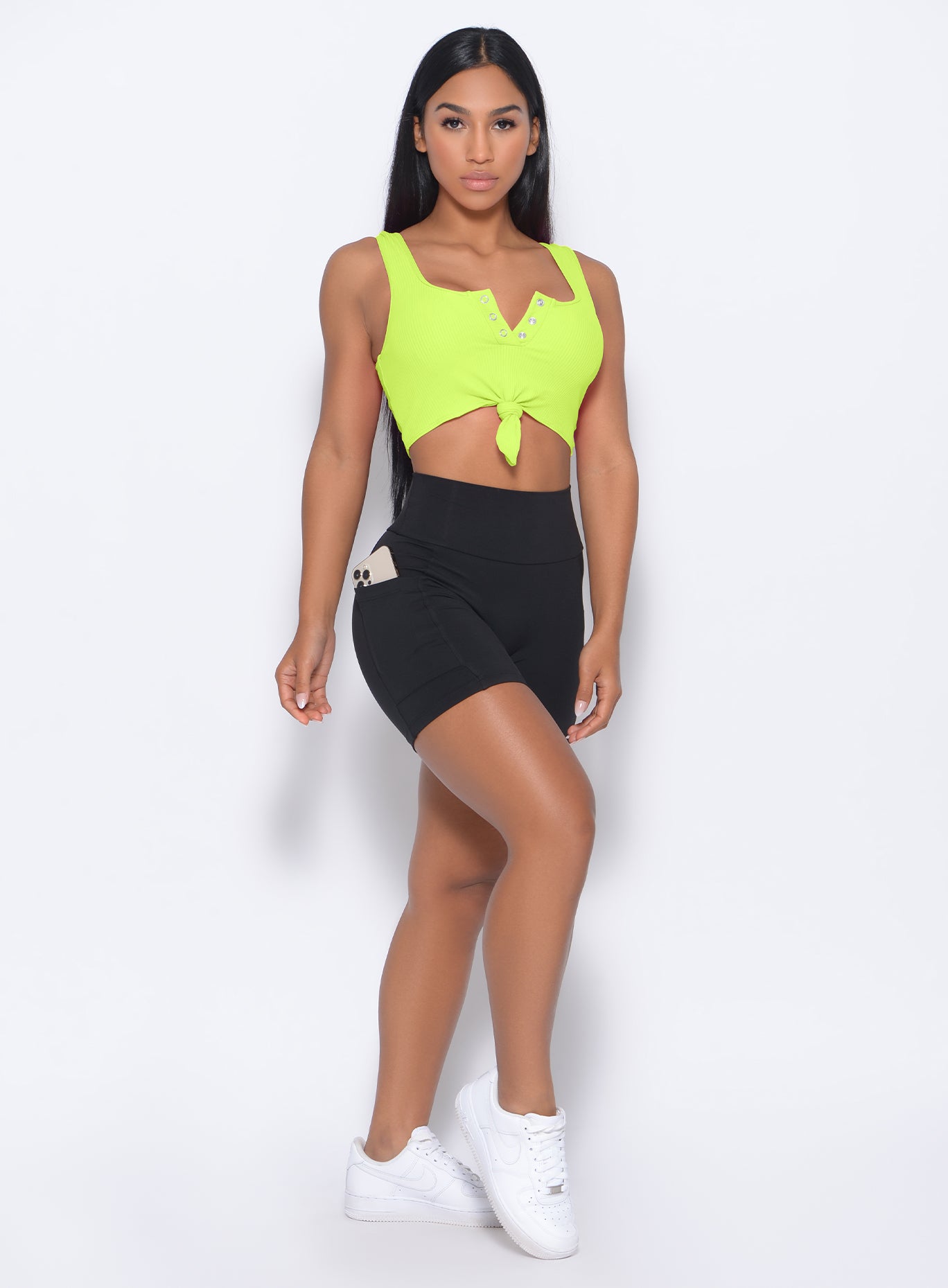 A picture of a model facing forward wearing our henley sports bra in neon yellow and a black shorts