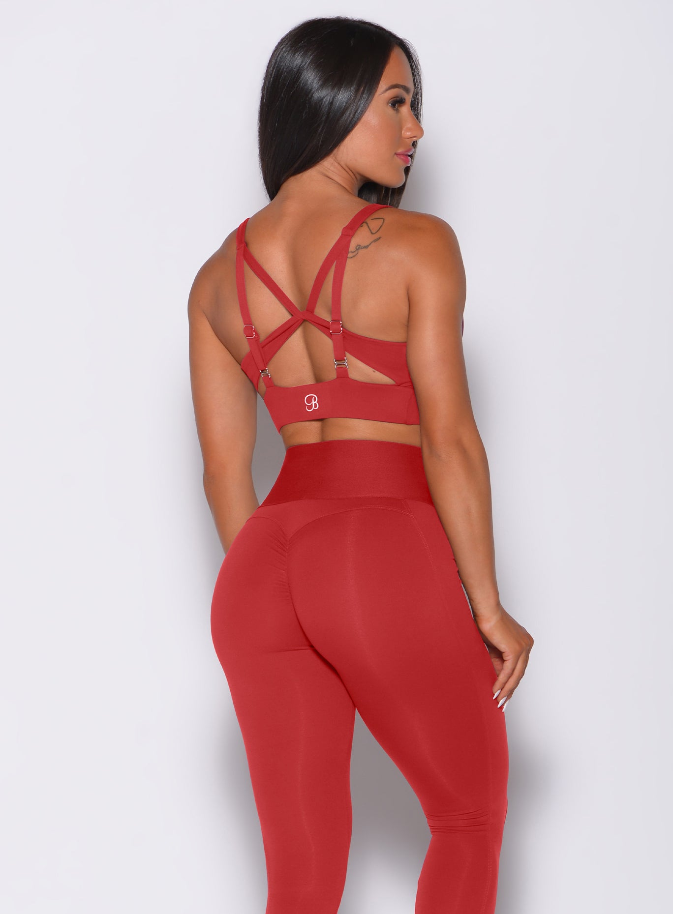 Back side profile view of a model in our impact sports bra in sunset red and a matching leggings