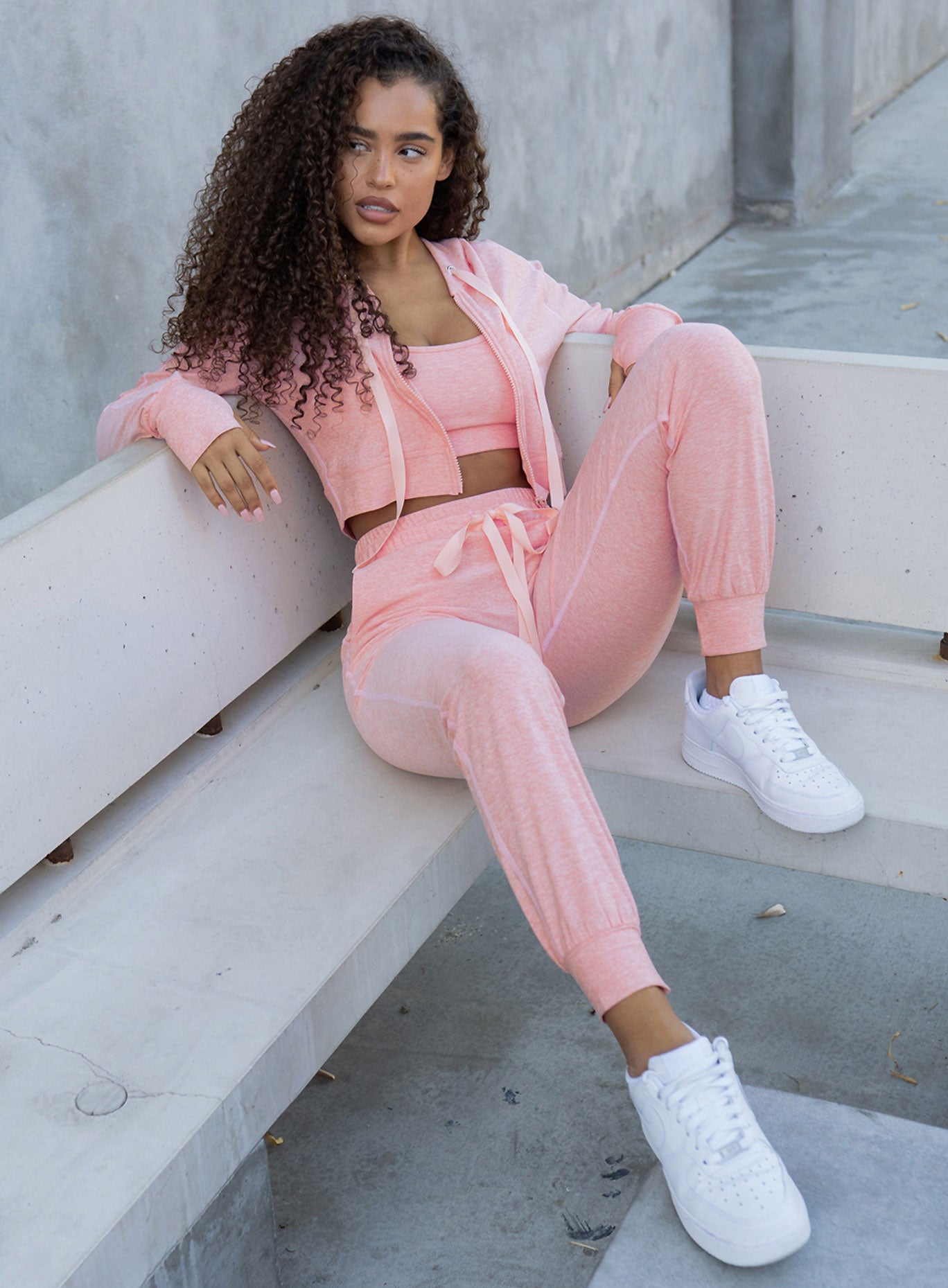 Picture of a model sitting on a bench wearing our  cozy joggers in peachy pink and a matching top  