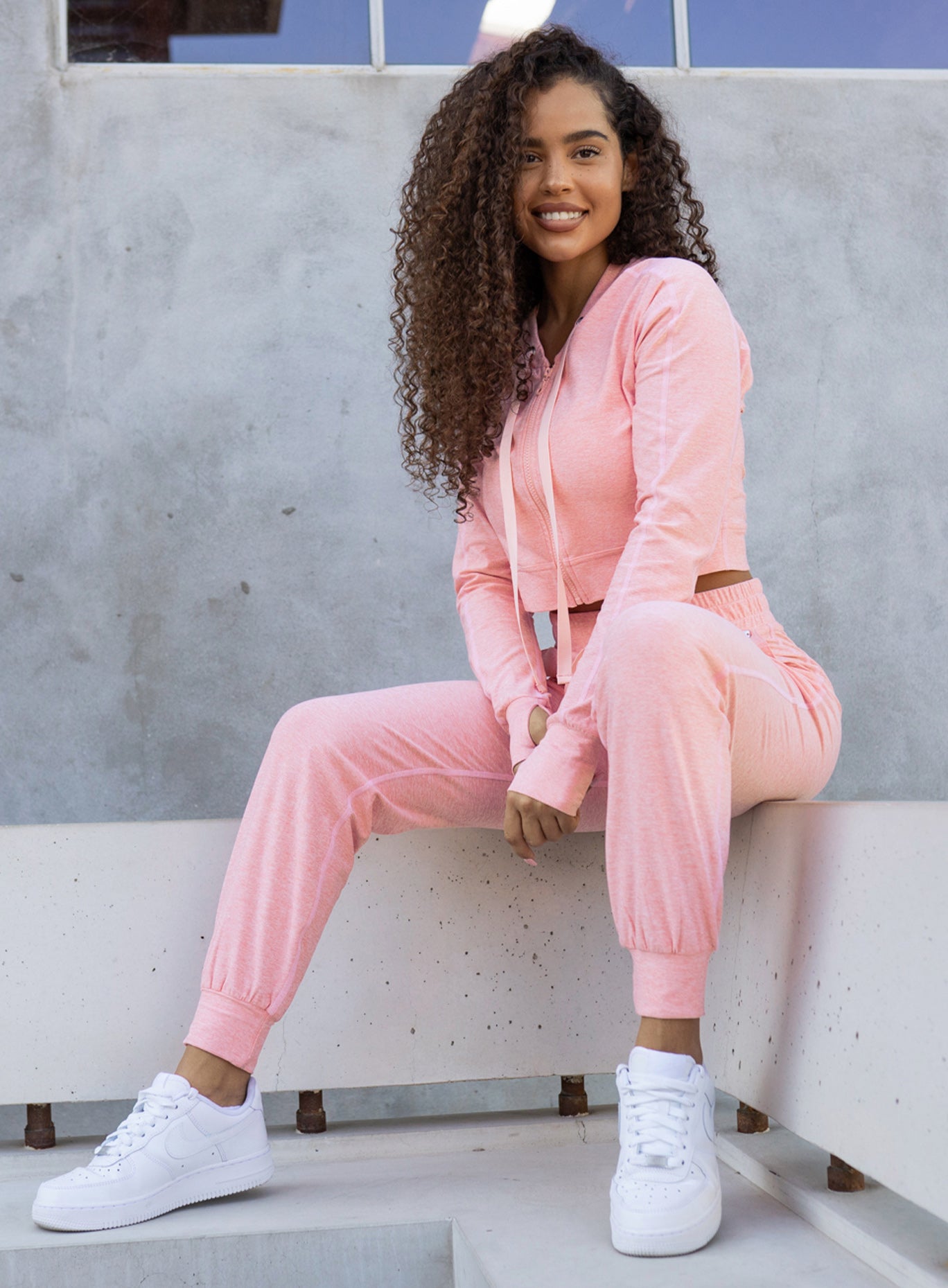 Picture of a model sitting on a bench wearing our cozy joggers in peach pink and a matching hoodie 