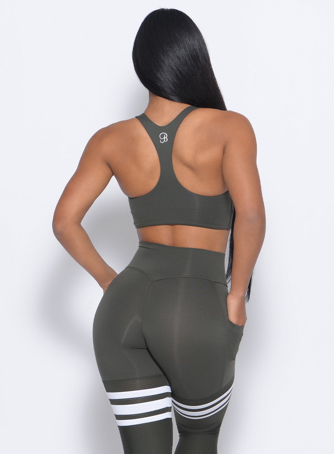 Back view of the model with her hand in pocket wearing our keyhole bralette in hunter green color and a matching leggings