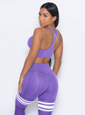 Left side view of the model facing to her left wearing our perform thigh highs in royal purple color with three white stripes on thighs and a matching bra