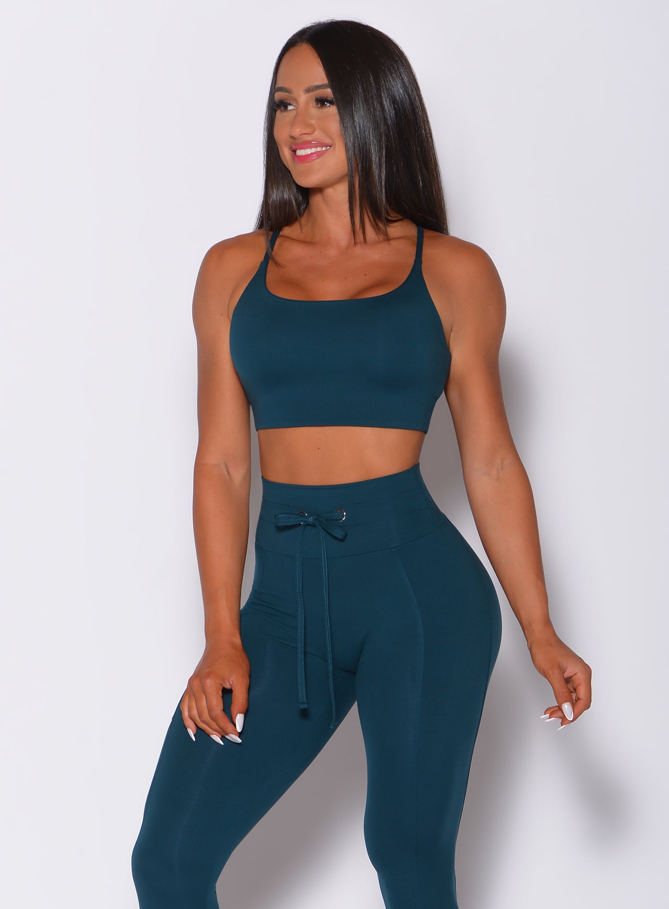 Front profile view of a model in our cross fit sports bra in peacock color and a matching leggings