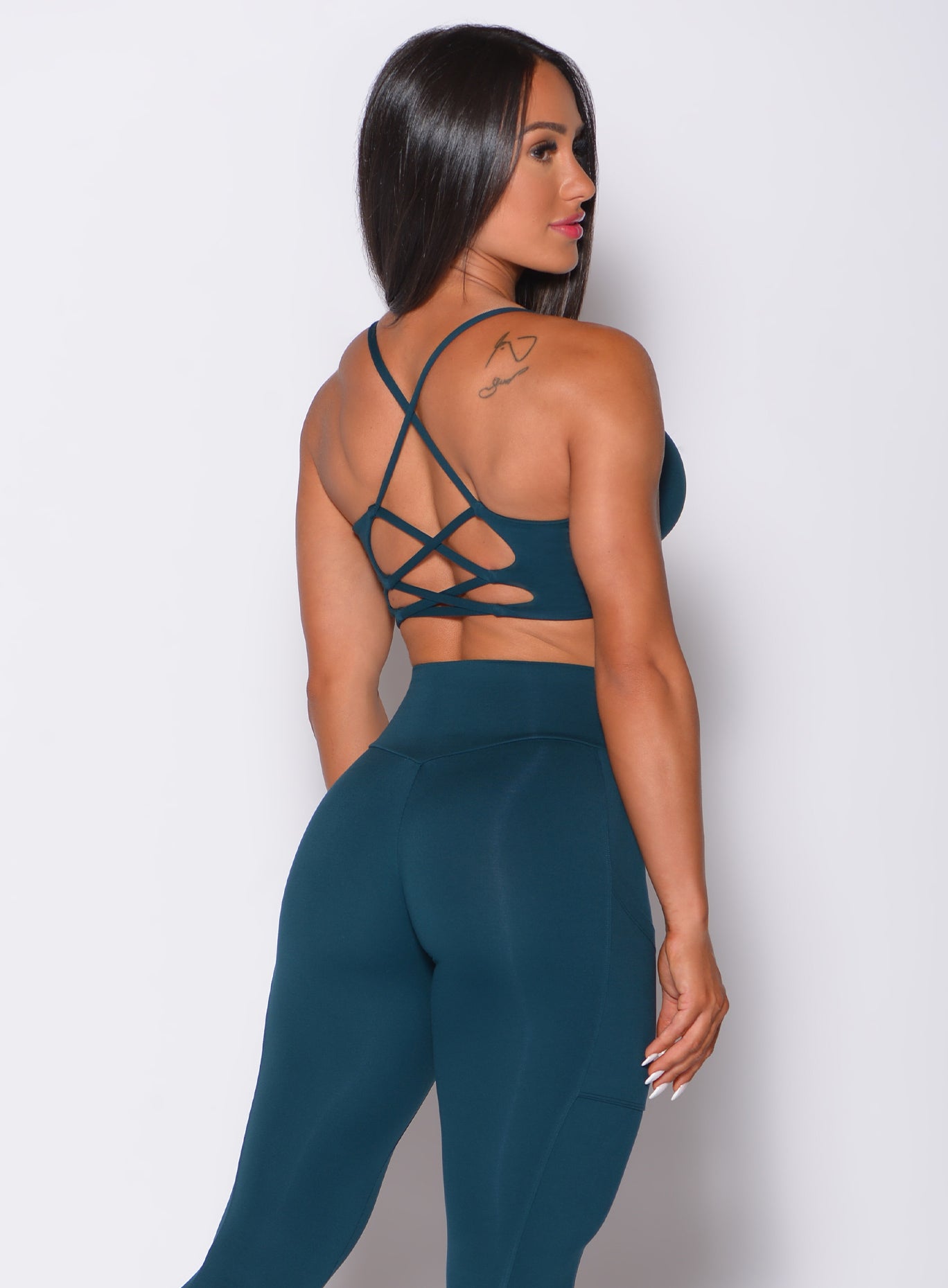 Back profile view of a model in our cross fit sports bra in peacock color and a matching leggings