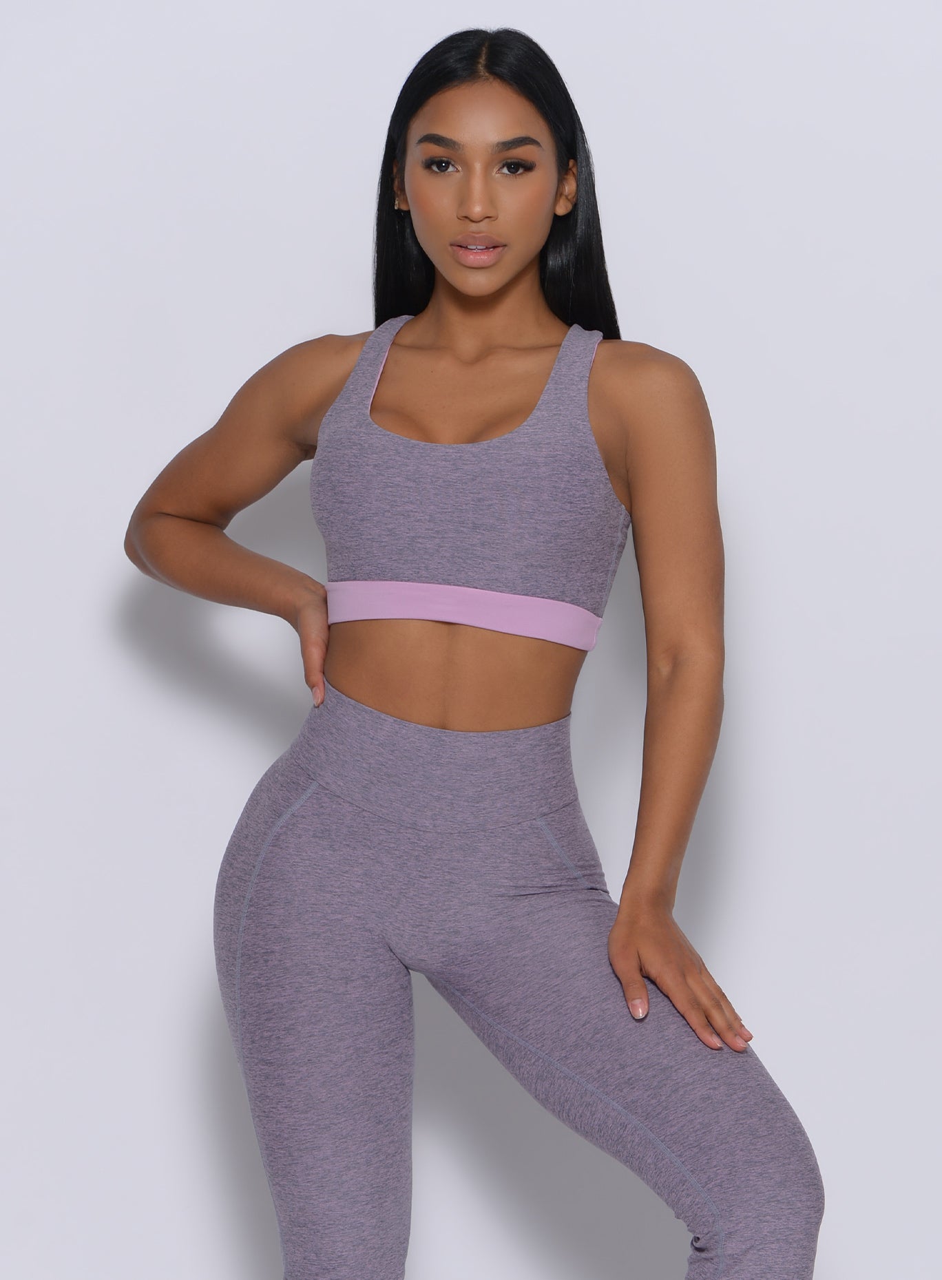 Front profile  view of the model with her right hand on waist wearing our reversible long bra in orchid color underneath a tank top in lavender color 