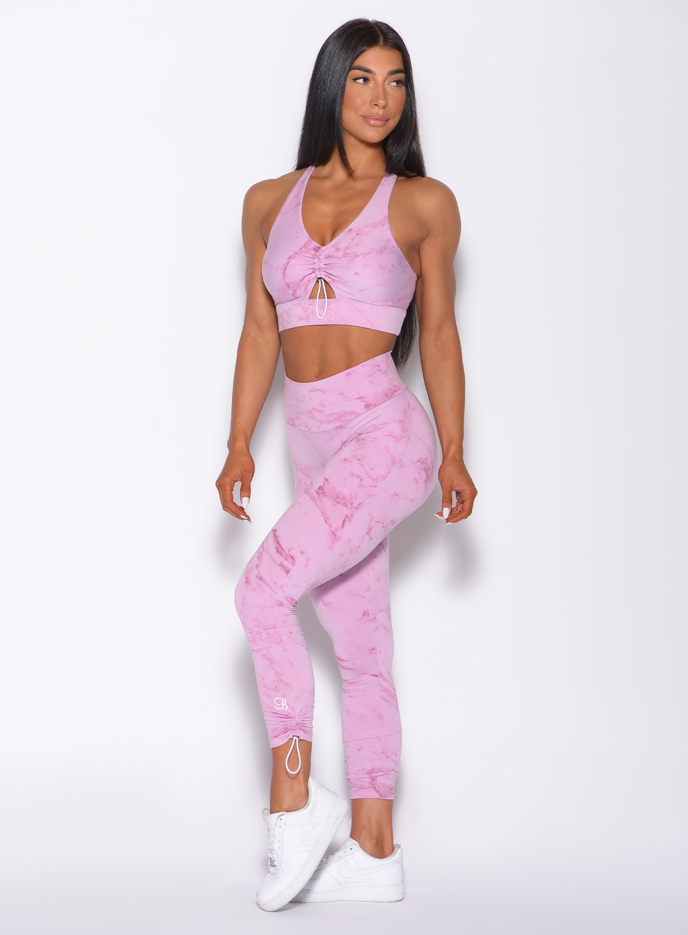 Left side profile view of a model angled to her left wearing our adjustable leggings in marble pink color and a matching bra