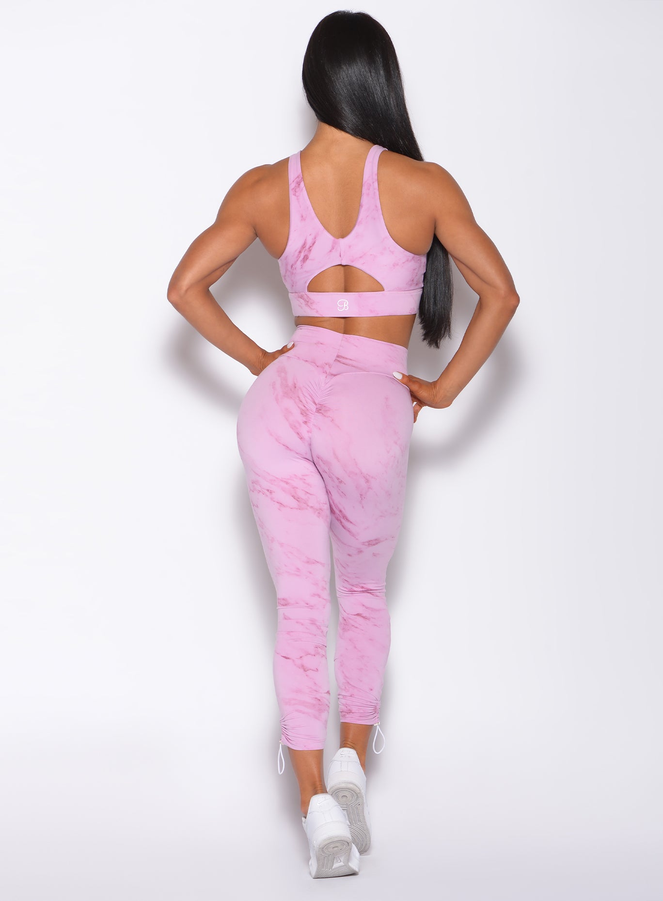 Back profile view of a model in our adjustable leggings in marble pink color and a matching bra
