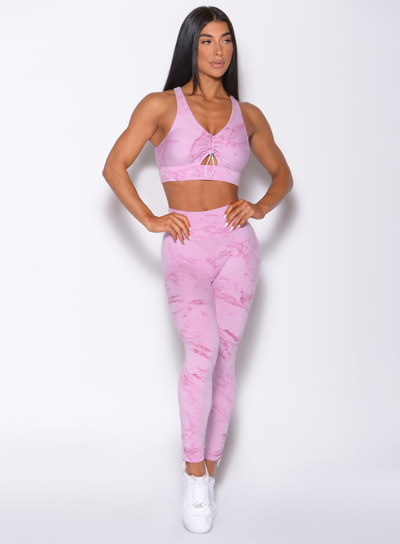 Front profile view of a model wearing our adjustable leggings in marble pink color and a matching sports bra