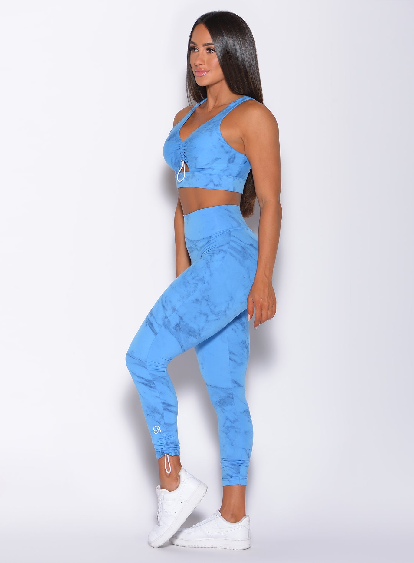 Left side profile view of a model wearing our adjustable leggings in blue marble color and a matching bra