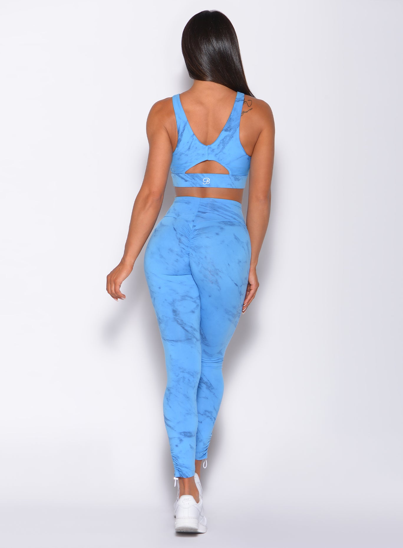 Back profile view of a model in our adjustable leggings in blue marble color and a matching bra