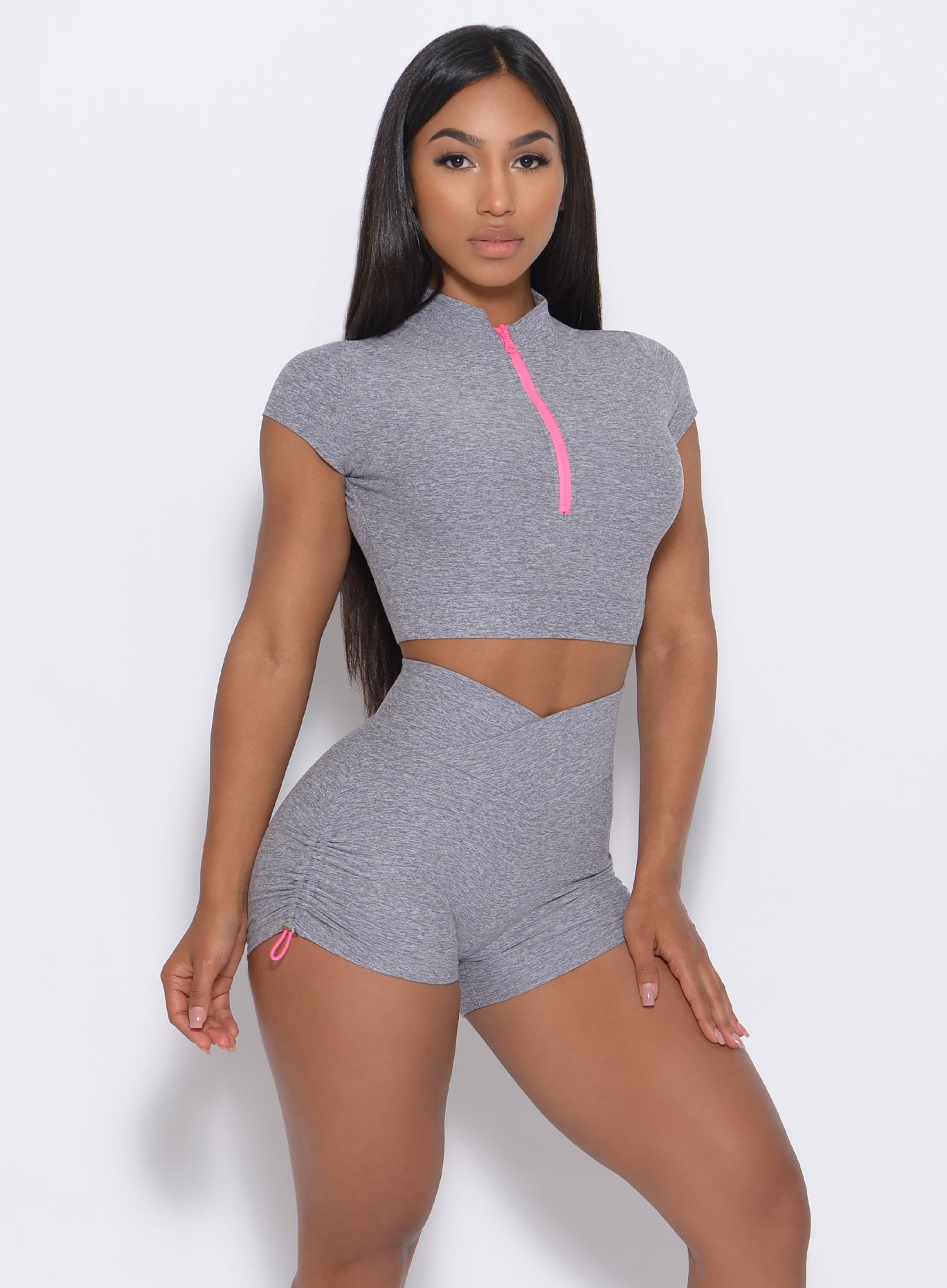 Front view of the model with her left hand on thigh wearing our neon zip top in cloud color and a matching shorts