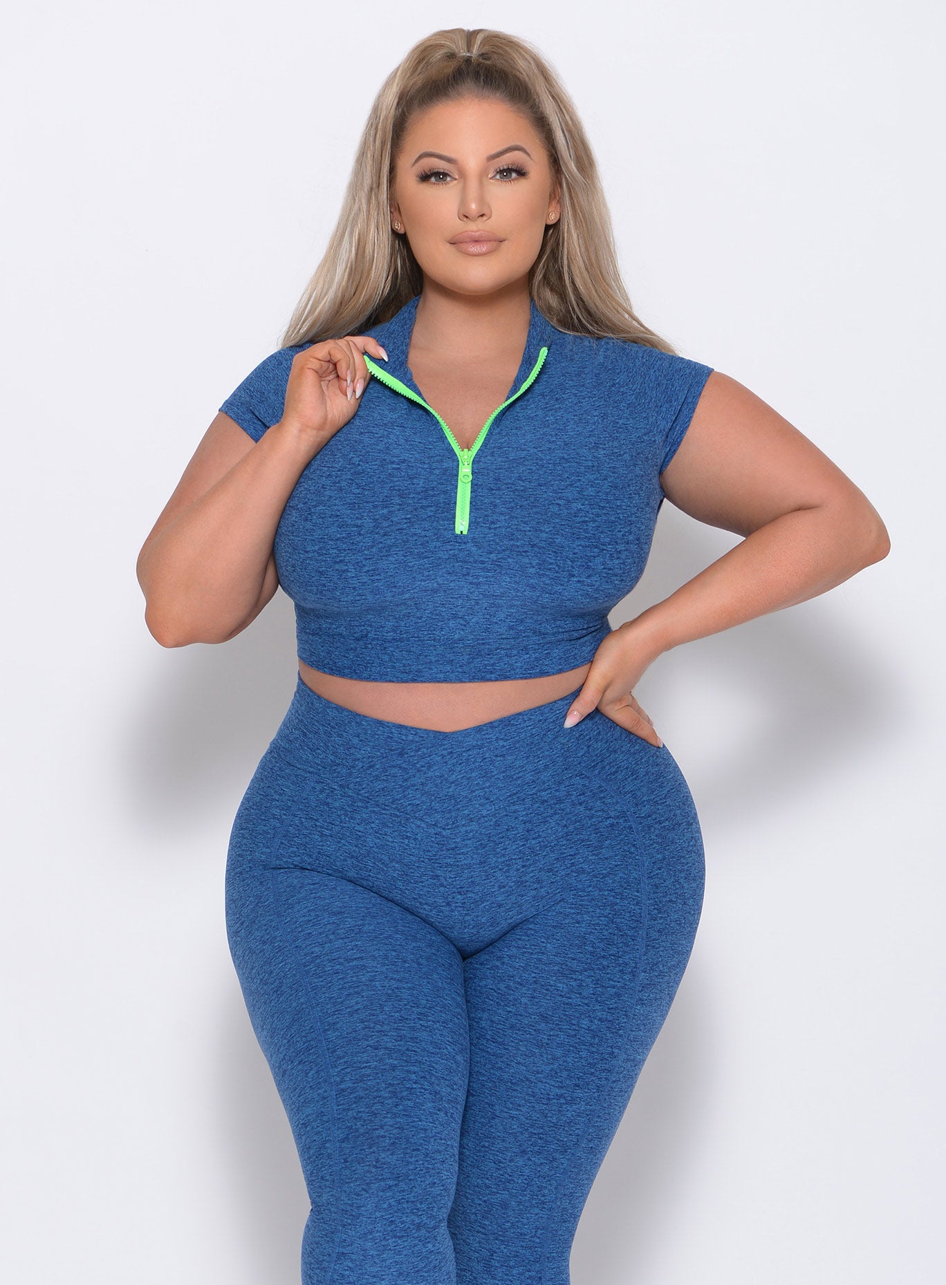 Model facing forward with her left hand on waist wearing our neon zip top in ocean color and a matching shorts