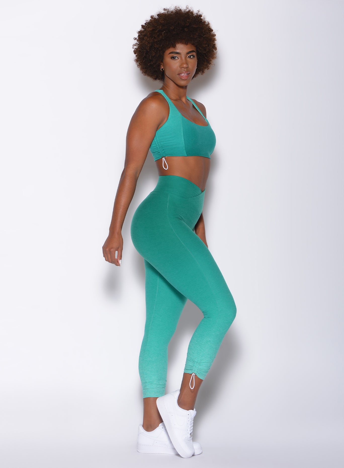 Right side profile view of a model facing to her left wearing our toggle leggings in Ombre Ibiza Green and a matching sports bra