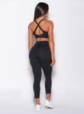Back profile view of a model in our black toggle leggings and a matching bra 