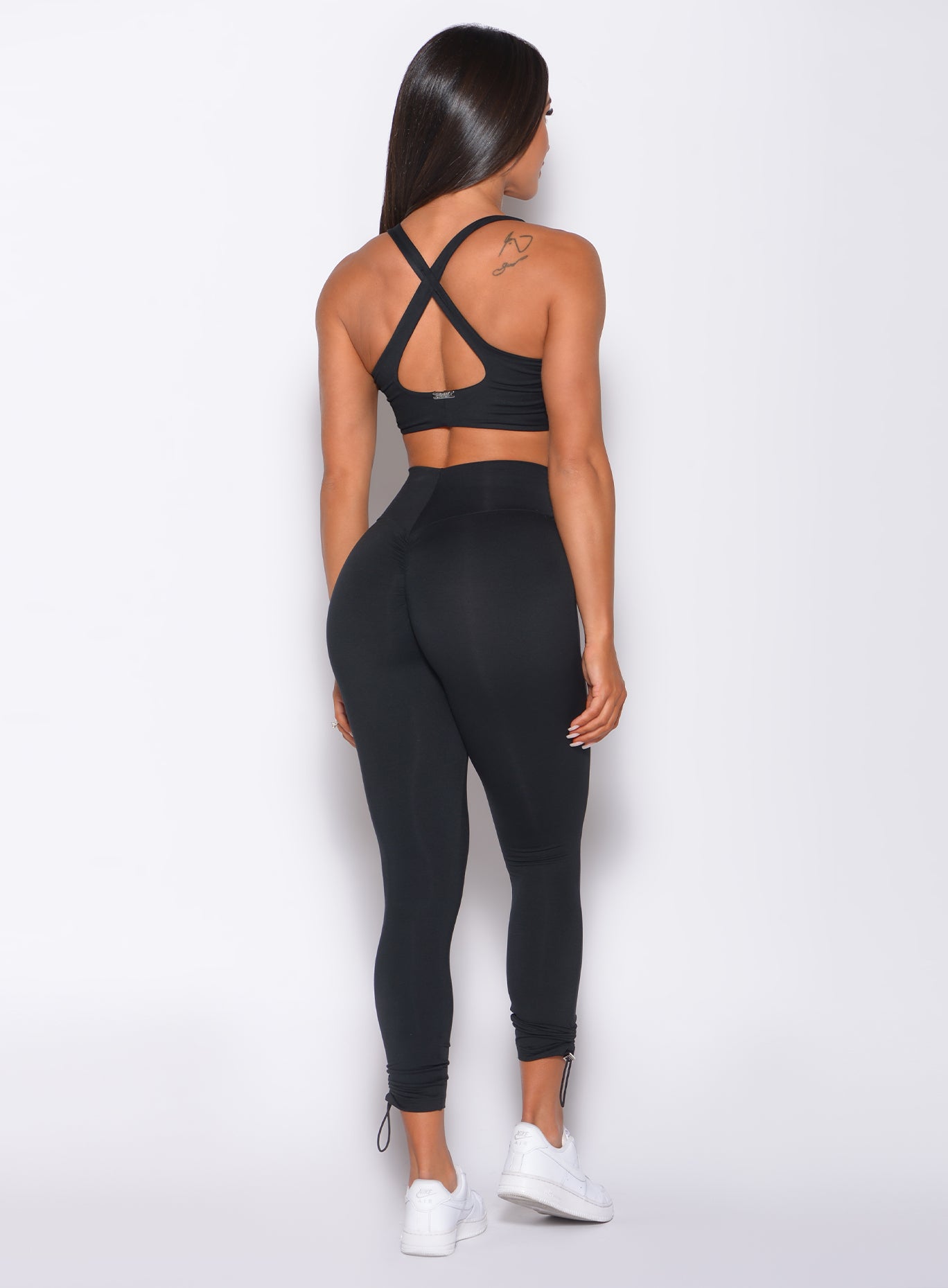 Back profile view of a model in our black toggle leggings and a matching bra 