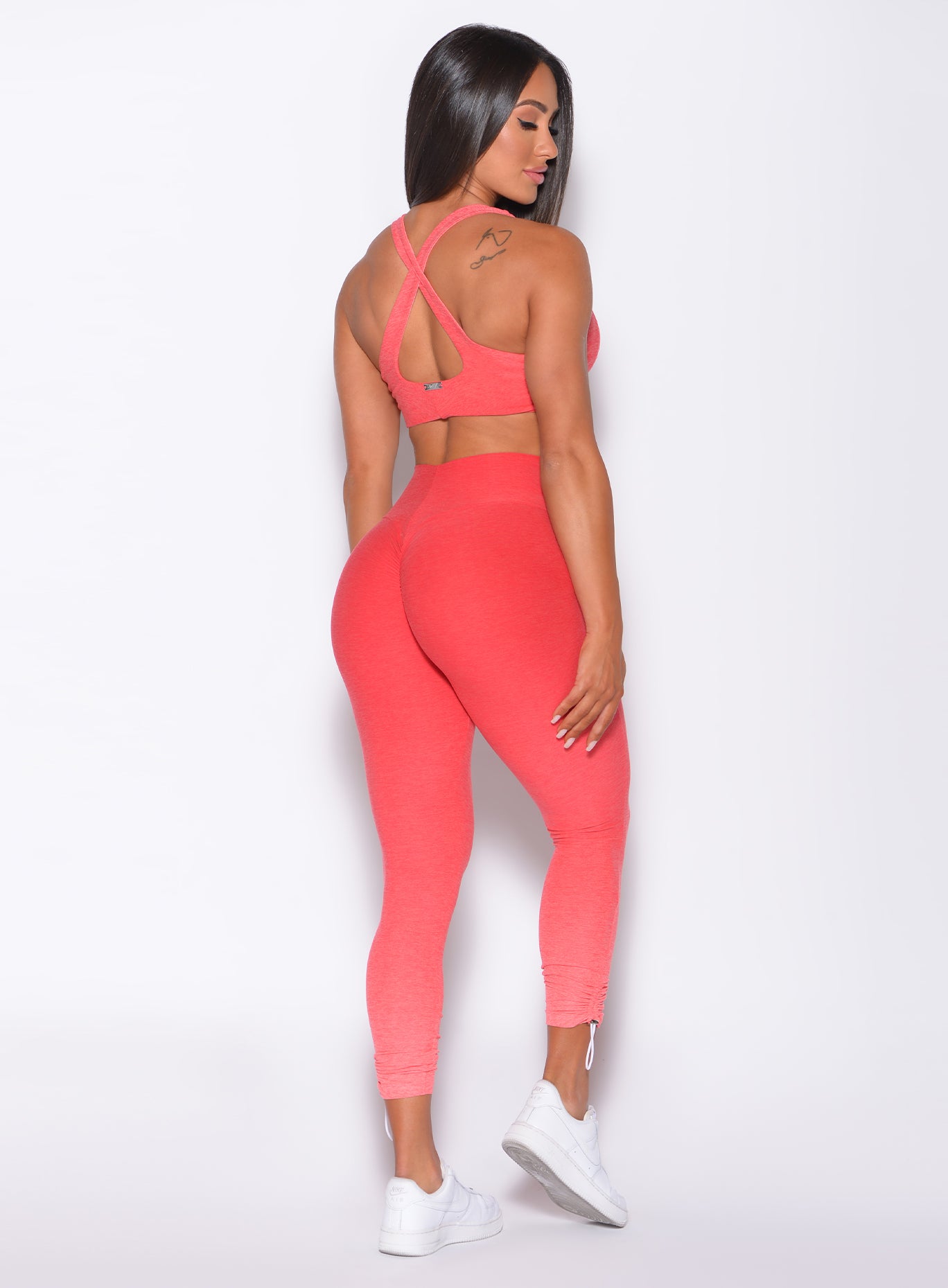 Back profile view of a model facing to her right wearing our toggle leggings in Ombre Fiji Coral and a matching bra