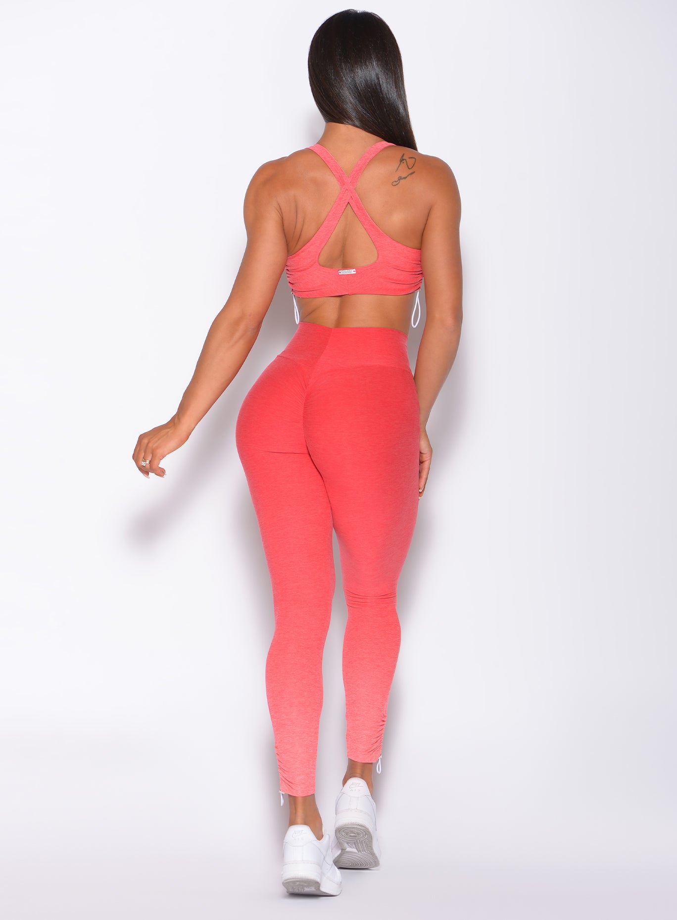 Back profile view of a model in our toggle leggings in Ombre Fiji Coral and a matching bra 