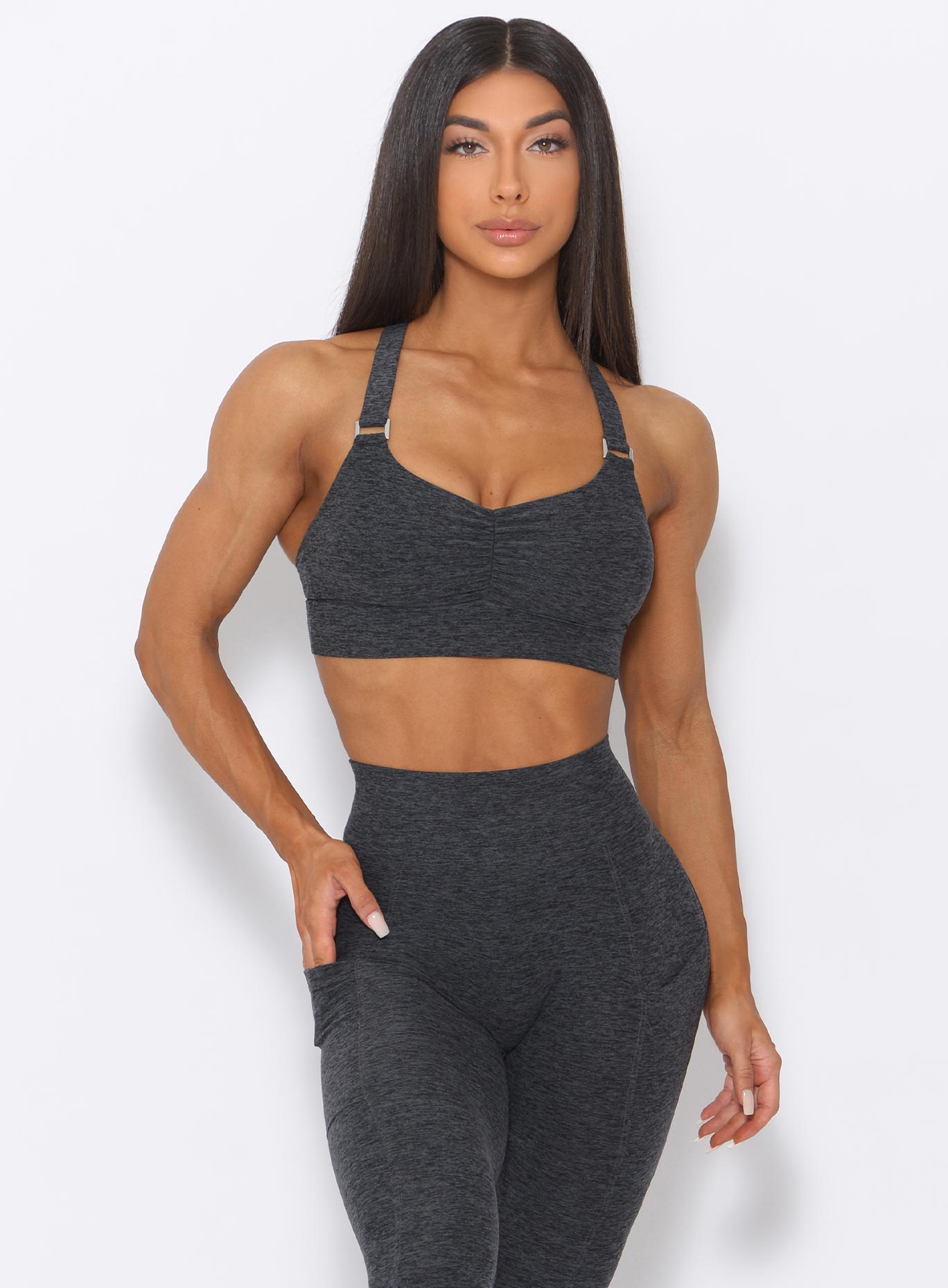Front view of the model with her right hand on waist wearing our perfection sports bra in charcoal color and a matching leggings