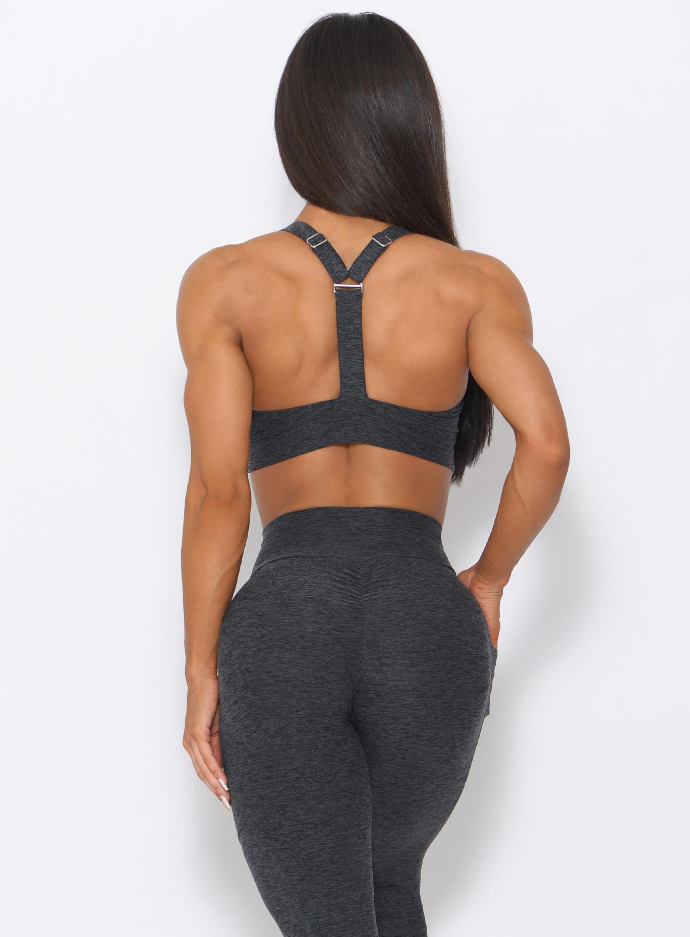 Back view of the model with her right hand on waist wearing our perfection sports bra in charcoal color and a matching leggings