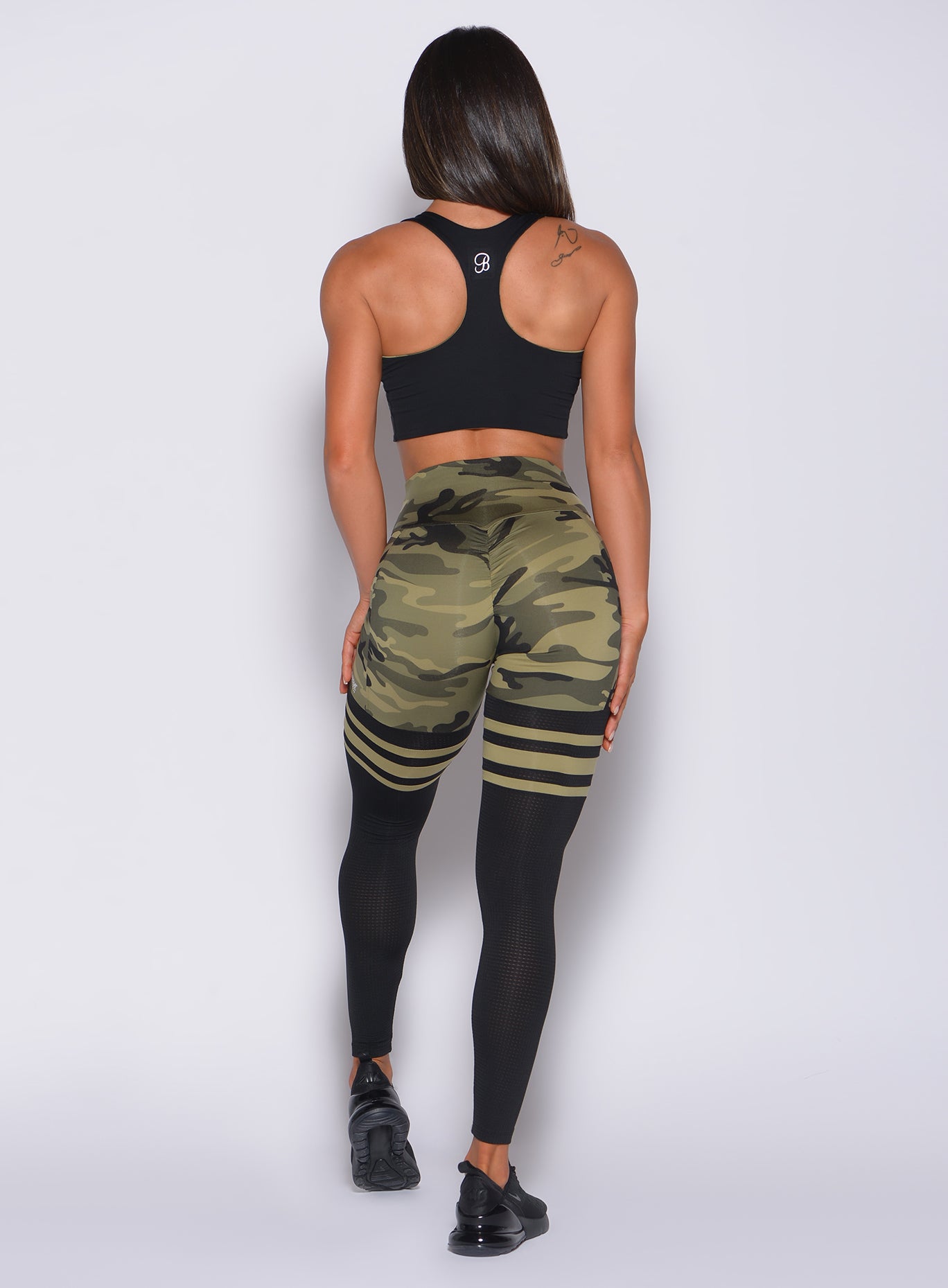 Back profile view of a model wearing our green camo scrunch thigh high and a black bra