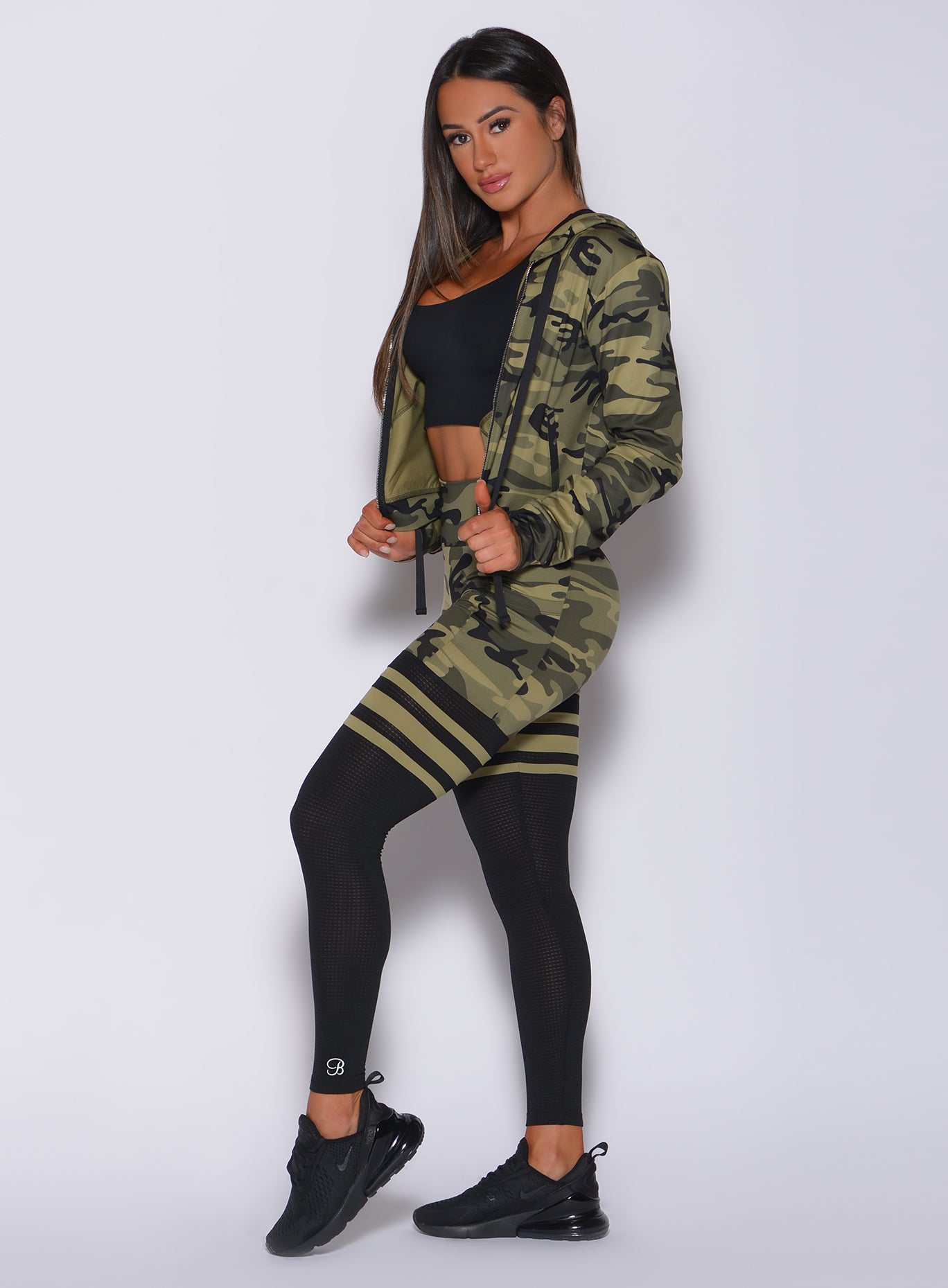 Left side profile view of a model angled left wearing our green camo scrunch thigh high and a matching jacket