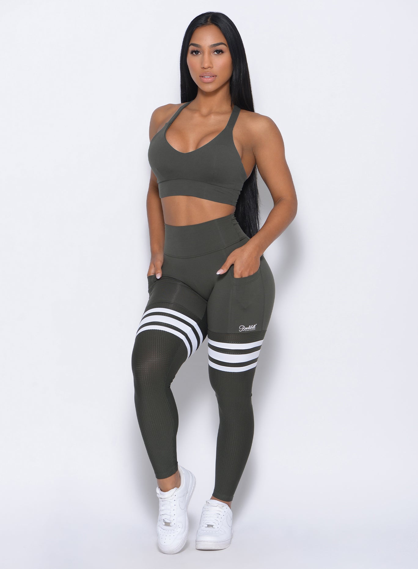 Front profile view of the model with her hands in pocket wearing our perform thigh highs in twilight blue color with three white stripes on thighs and a matching bra