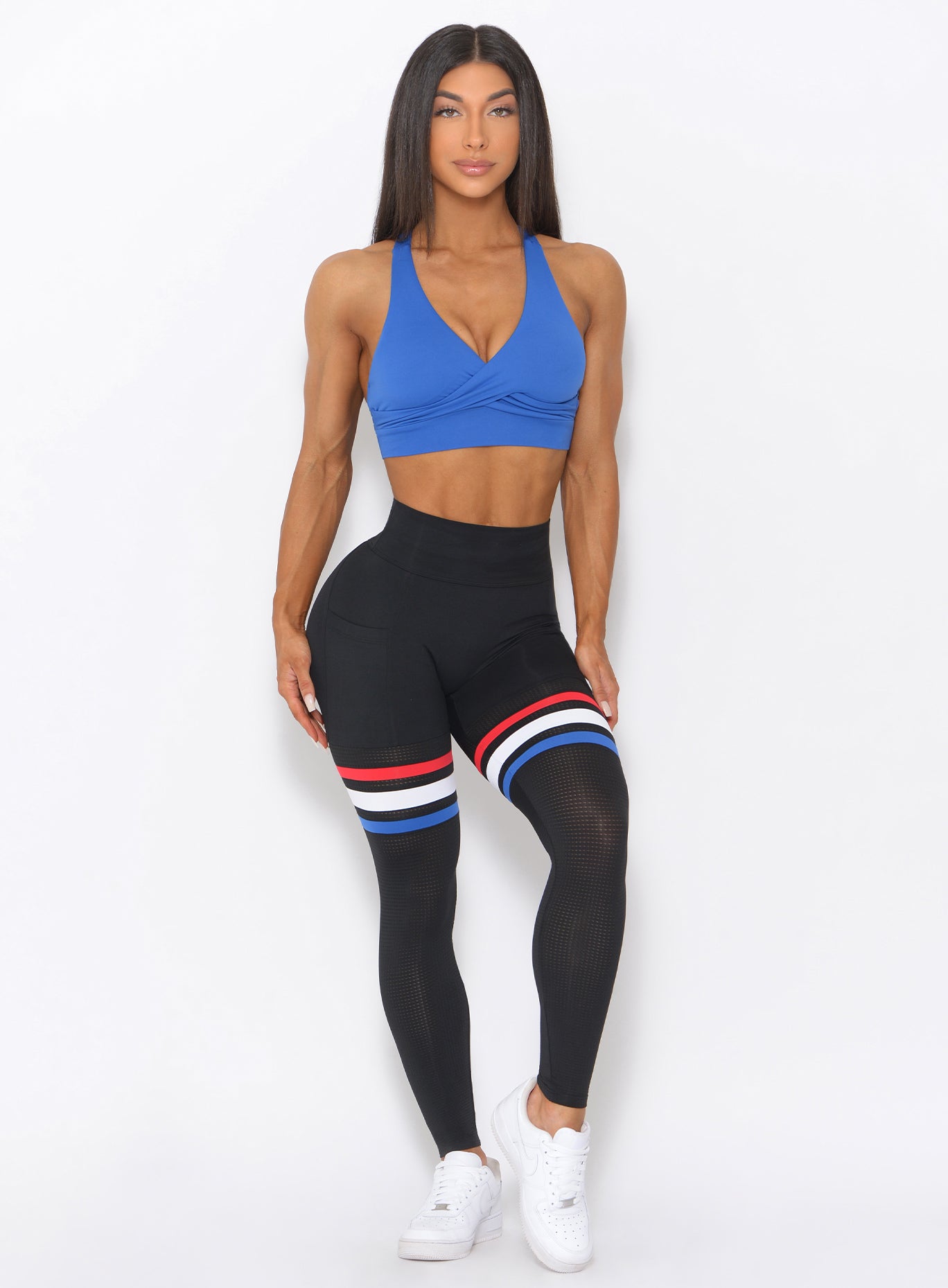 Full front view of the model wearing our blue sports bra and a black high waist thigh high leggings with three stripes on thighs