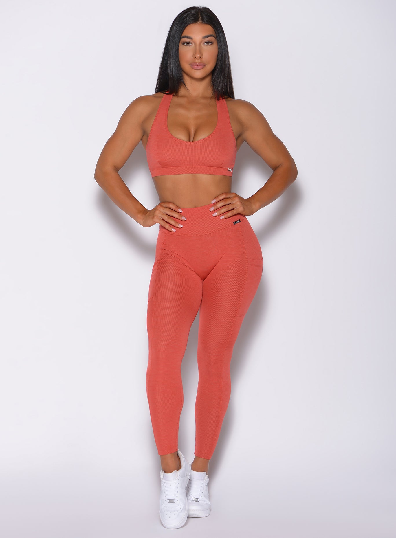 Front profile view of a model in our pocket rib leggings in burnt orange color and a matching bra