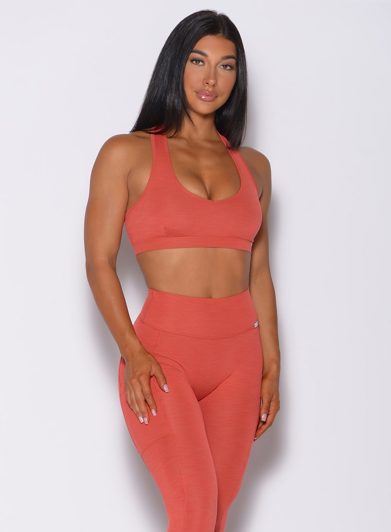 Right side profile view of a model wearing our power rib sports bra in burnt orange color and a matching high rise leggings
