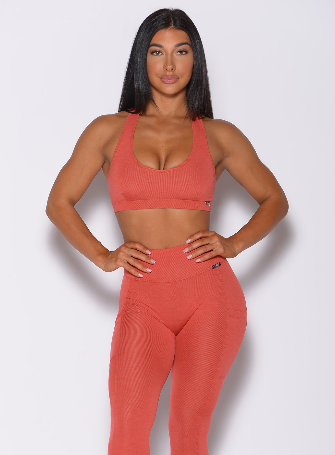 Front profile view of a model in our power rib sports bra in burnt orange color and a matching leggings