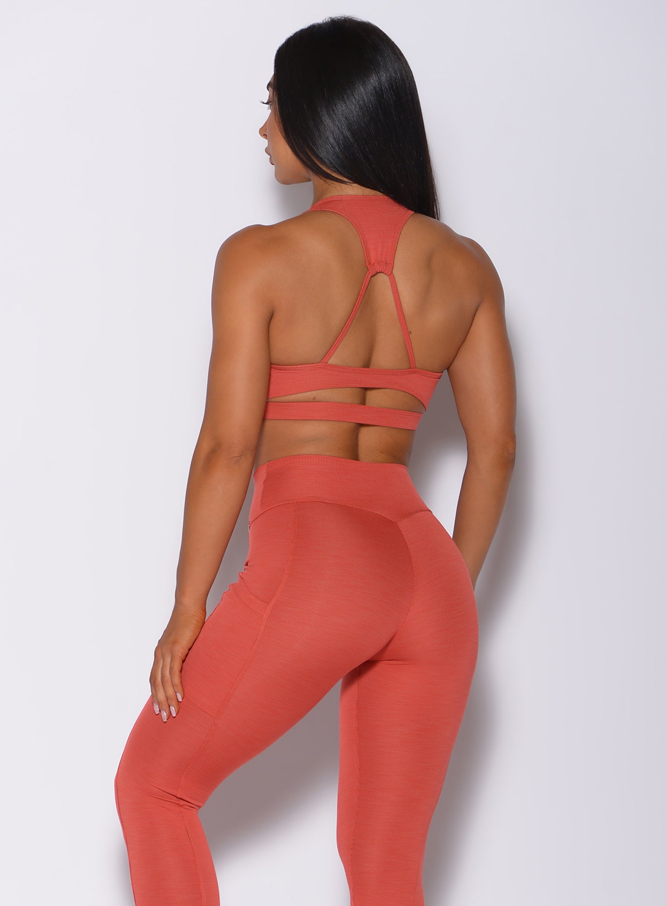 Back profile view of the model in our power rib sports bra in burnt orange color and a matching leggings